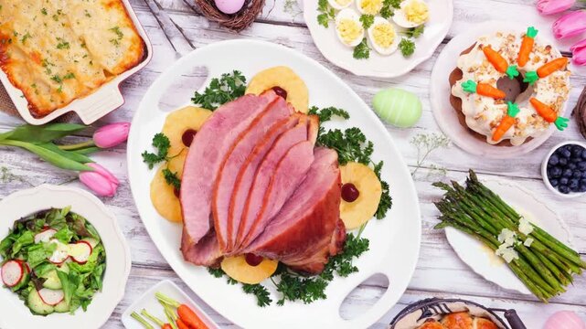 Classic Easter ham dinner. Slow rotating zoom motion. Overhead view table scene on a white wood background.