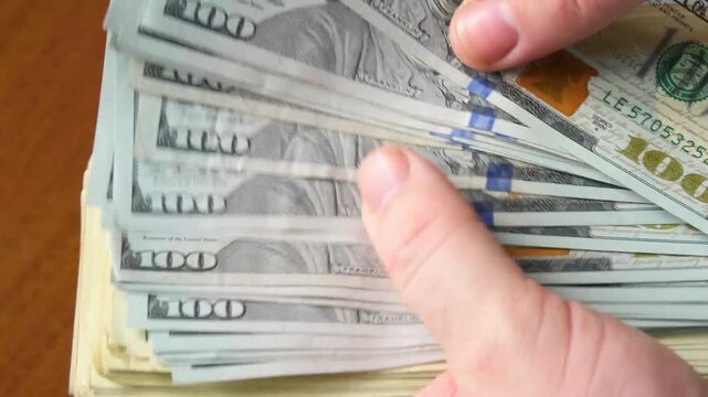 Close-up of a hand counting stacks of hundred dollar bills