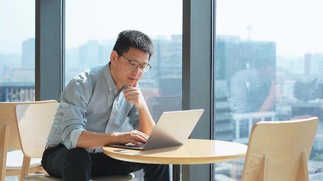 Man working on a laptop computer by the window in a modern office setting