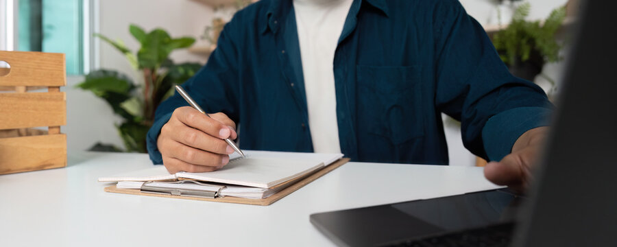 A man is writing in a notebook while sitting at a desk