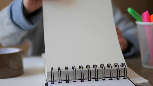 Blank, textured page in a spiral-bound sketchbook opened by a student