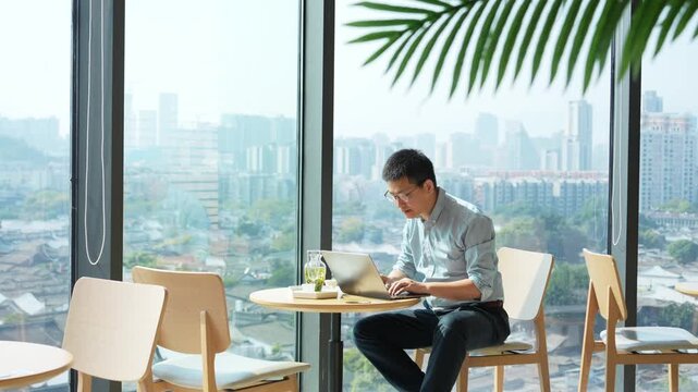 A young man reading and working attentively at a coffee table by the window in a modern urban office space