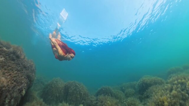 Freediving, Snorkeling, Woman, swims powerfully underwater over an algae-covered reef on a sunny tropical day