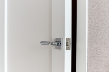 A sleek metallic door handle with a square base mounted on a white interior door. Features a simple...