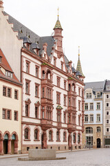 Fototapeta premium A large building in Leipzig Germany with a stone base and a stone statue in front of it. The building is white and has a red roof. The street is empty and the sky is cloudy
