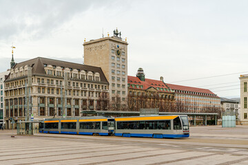 Obraz premium A yellow and blue train is parked in front of a large building in Leipzig Germany. The train is surrounded by a lot of empty space, giving the impression of a quiet and peaceful scene