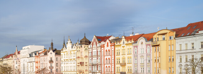 Fototapeta premium A row of colorful buildings with a cloudy sky in the background in Pilsen city in Czech Republic. The buildings are tall and have many windows