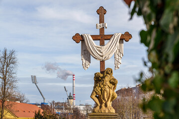 A cross with a white cloth draped over it is in front of a building in city Pilsen in Czech Republic. The cross is surrounded by a white cloth and has the letters JH on it
