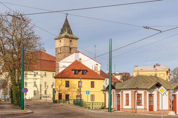 Obraz premium A small town with a yellow building and a red roof in city Pilsen in Czech Republic. The buildings are old and the street is lined with trees