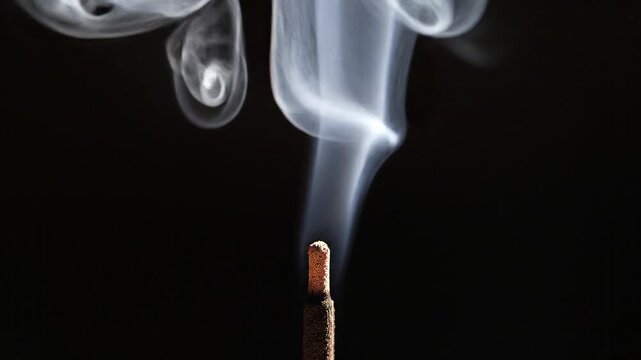 Close-up of burning cigarette emitting smoke on dark background