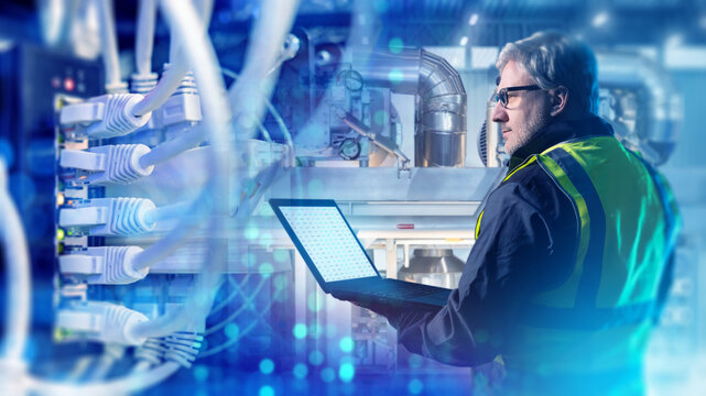 Industrial automation, engineer monitors equipment and network connections on a laptop, supervising smart manufacturing systems, data flow, and technical maintenance.