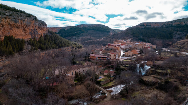 High-angle scenic view of the charming village of Calmarza, surrounded by rolling hills and forests under a dramatic cloudy sky, a perfect example of a tranquil rural destination in Aragon, Spain.