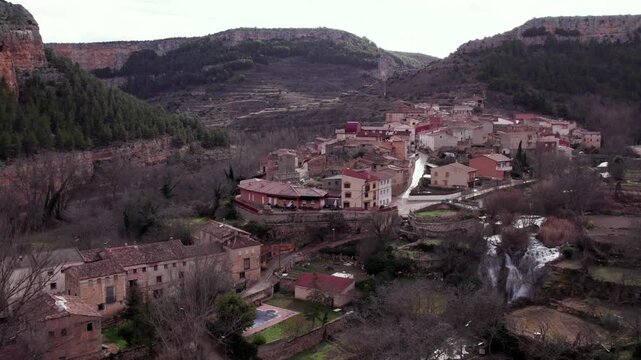Panoramic aerial view of the picturesque village of Calmarza nestled in a green valley, showcasing traditional Spanish architecture under a partly cloudy sky in the province of Zaragoza, Spain.