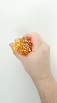 Single hand squeezes a transparent gold bead stress ball, compressing the gel beads then releasing so it slowly rebounds on a clean white background. Repeated squish pops create calming ASMR.