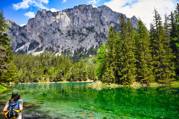 A girl with a backpack is looking at a Green lake, Austria, springtime