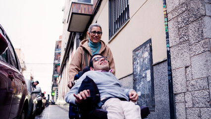 Woman pushing man in an electric wheelchair, navigating a city street together. Focusing on care and mobility support © DMegias