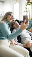 Mother and son happy on a couch taking a selfie with a smartphone. Man with mobility disability and a woman smiling, sharing a moment