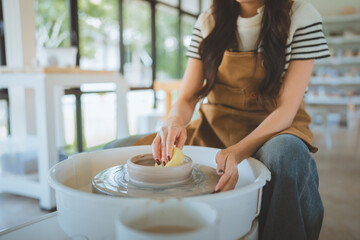 Close-up of hands of female artist shaping wet clay on spinning pottery wheel with sponge &ndash; creative ceramic making process in modern craft studio, traditional handmade sculpting technique