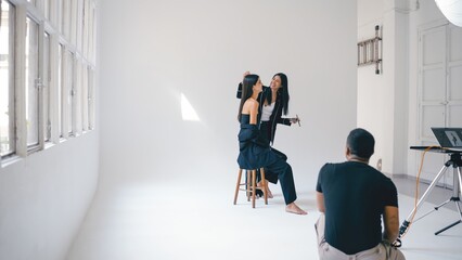 Makeup artist applying makeup on beautiful model while photographer taking photos in professional studio