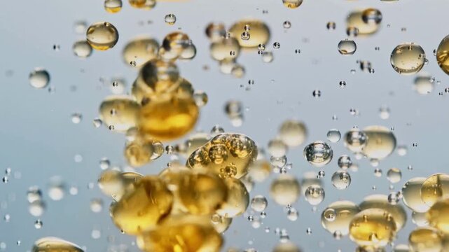 Golden bubbles of varying sizes rise in clear liquid against a soft blue background, creating a sense of lightness and effervescence.