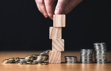 Hand builds wooden blocks beside coin stacks
