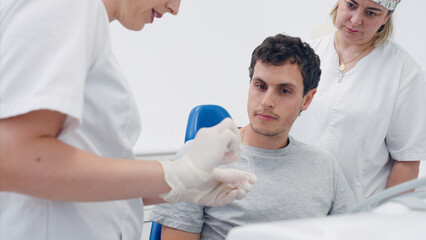 Obraz premium Dentist in protective gloves explaining clear aligner treatment to a young male patient in a dental clinic