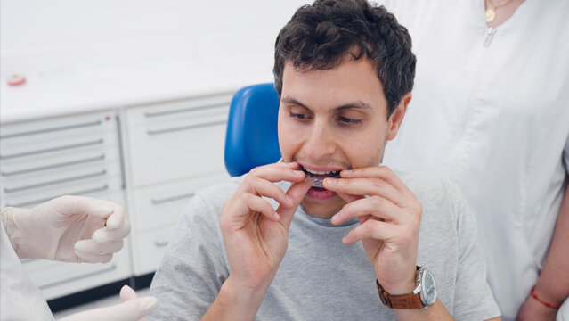 Patient at a dental clinic trying on a transparent plastic aligner, guided by unidentifiable healthcare professionals