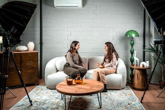 Two women hosting a podcast, conversing in a professional studio setting with cameras and lighting equipment