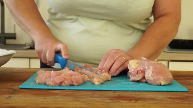 Woman cutting chicken fillet for cooking

