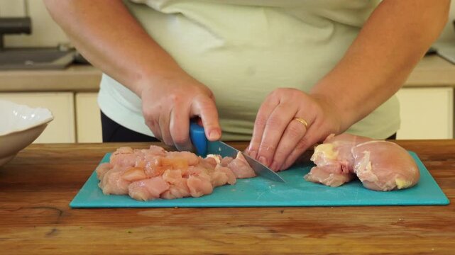 Woman cutting chicken fillet for cooking
