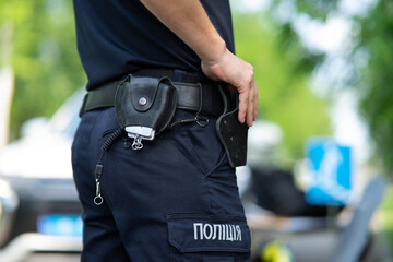 Ukrainian patrol police officer in dark blue trousers with "Police" lettering, demonstrating a tactical duty belt with professional equipment.
