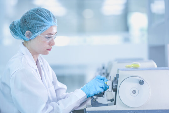 Medical pathologist preparing biopsy slide for cancer diagnosis. Doctor in protective gear using microtome machine to analyze tissue sample in hospital.