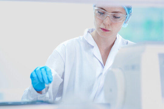 Professional histology technician cutting tissue section with rotary microtome. Female scientist in safety gear processing paraffin biopsy block in lab room.