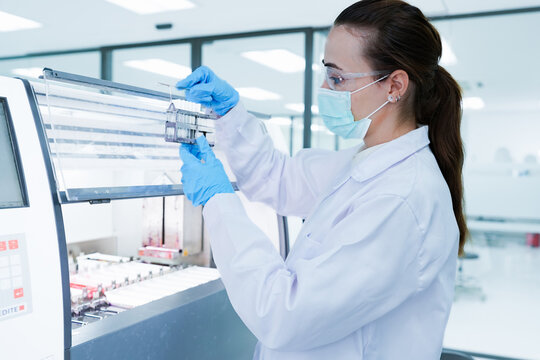 Medical scientist loading slide rack into automated stainer machine. Lab technician in protective gear processing histology samples in sterile hospital laboratory.
