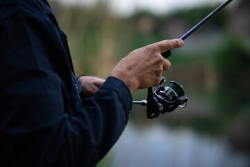 Close-up of a man's hand holding a spinning rod while fishing on the river, focus on the fishing tackle and grip.