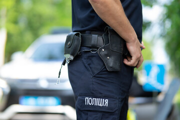 Ukrainian patrol police officer in dark blue trousers with "Police" lettering, demonstrating a tactical duty belt with professional equipment.