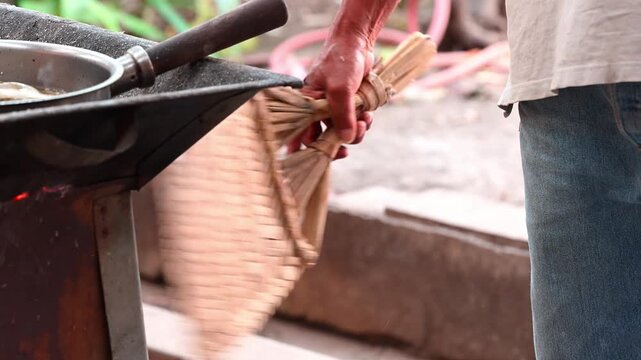 Close-up of a man's hand holding a handwoven palm leaf blower