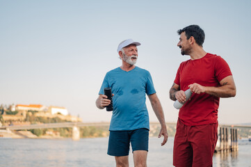 Senior man and personal trainer walking by river after workout