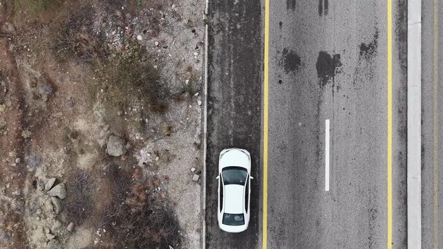 Aerial view of a white vehicle parked along a road with visible tire marks and patches on the asphalt surface