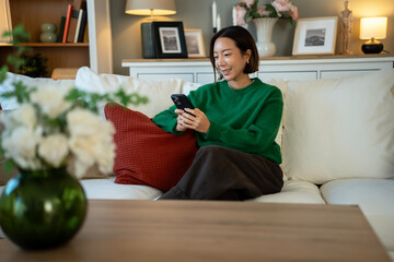 Obraz premium Young woman relaxing on sofa using smartphone at home