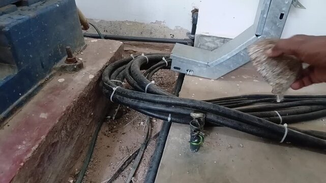 Close-up of dangerously exposed three-phase electrical wire terminals unsafely covered by a makeshift coconut shell on a factory floor, highlighting workplace hazards.
