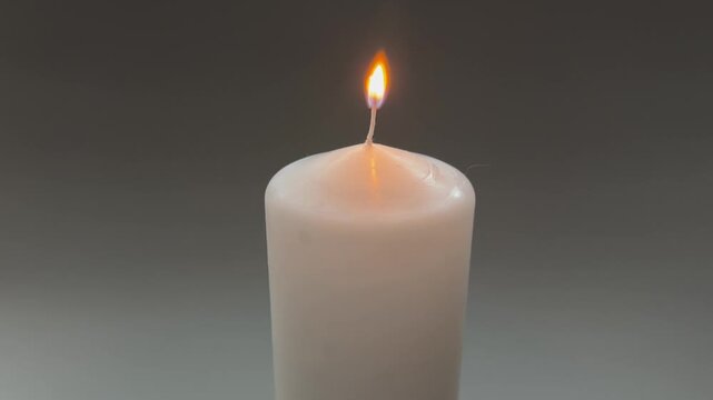 Burning white paraffin thick round candle on gray background