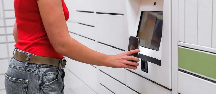 Contactless delivery: a woman uses smartphone to open a smart parcel locker for click-and-collect pickup. Modern last-mile e-commerce self-service returns and 24/7 convenience for urban shoppers now.