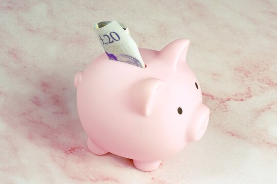 A pink piggy bank with a 20 pound note stuck in it.