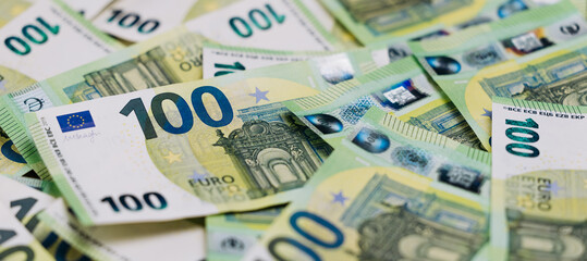 Naklejka premium Close-up view of scattered 100 euro banknotes displaying intricate designs and security features, emphasizing the currency's value and European monetary system