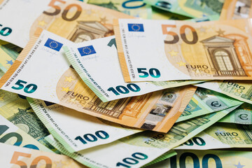 Obraz premium Close-up view of assorted Euro banknotes including 50 and 100 denominations stacked together on a flat surface, showcasing detailed designs and colors