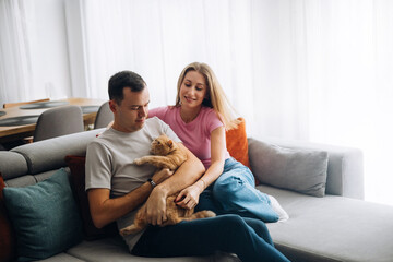 Obraz premium Couple sits on couch with a cat in a cozy living room during a sunny afternoon