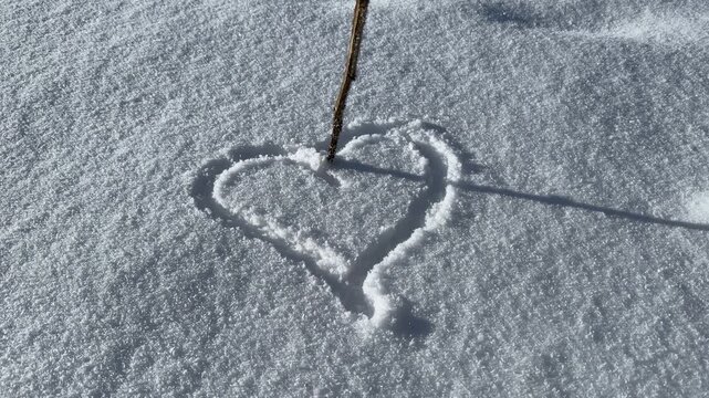 Drawing heart shape in snow with stick, winter love concept

