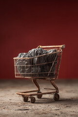 Metal shopping cart overflowing with crumpled brown paper bags against a dark brown background, representing sustainable packaging or recycling issues.