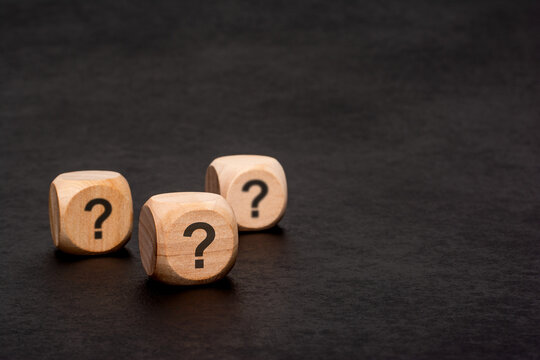 Three wooden cubes with question marks on black background
